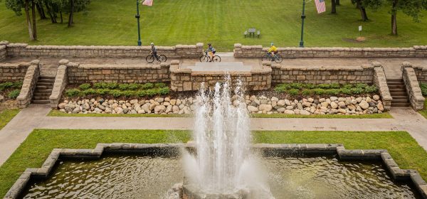 Three cyclists ride next to a fountain in Olcott Park, Virginia, MN