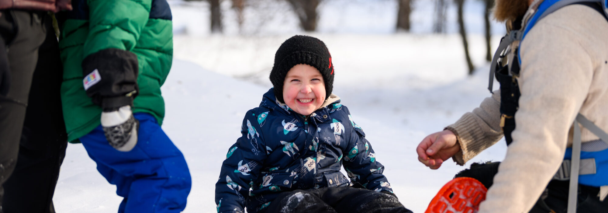 A little boy smiles as his dad puts snowshoes on him in northern Minnesota at Minnesota Discovery Center in Chisholm
