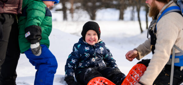 A little boy smiles as his dad puts snowshoes on him in northern Minnesota at Minnesota Discovery Center in Chisholm