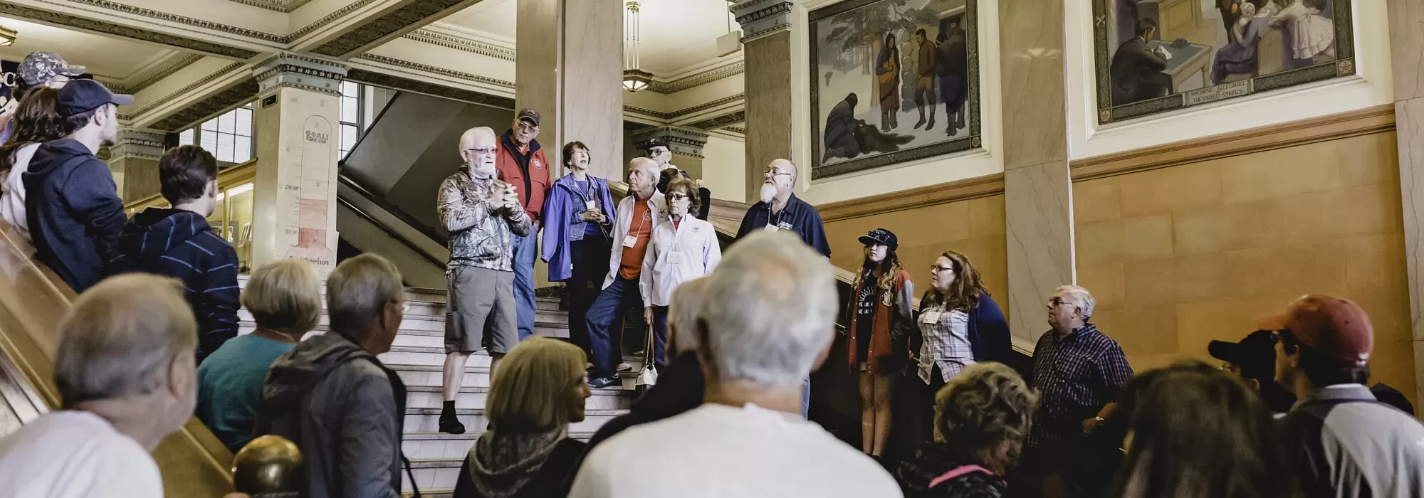 A group of men and women listens to a tour guide at Hibbing High School