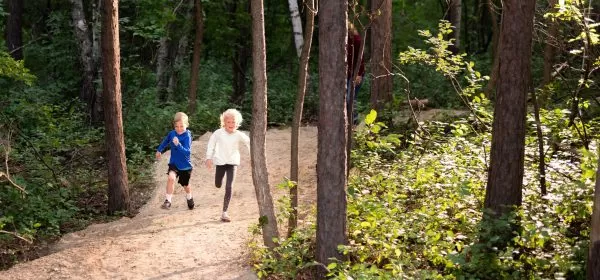 Two young children run joyfully among tall trees on a trail in northern Minnesota.